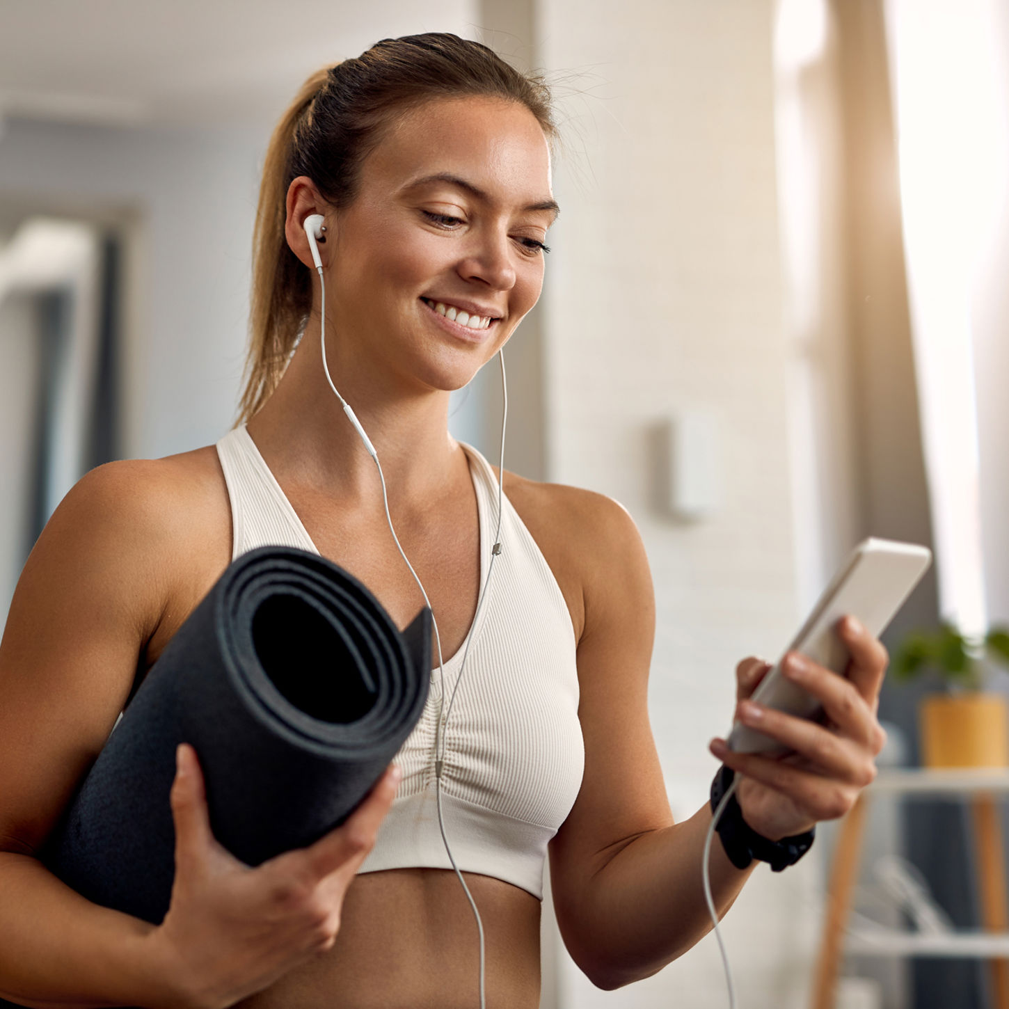 Happy Female Athlete Holding Exercise Mat While Texting Mobile Phone Home